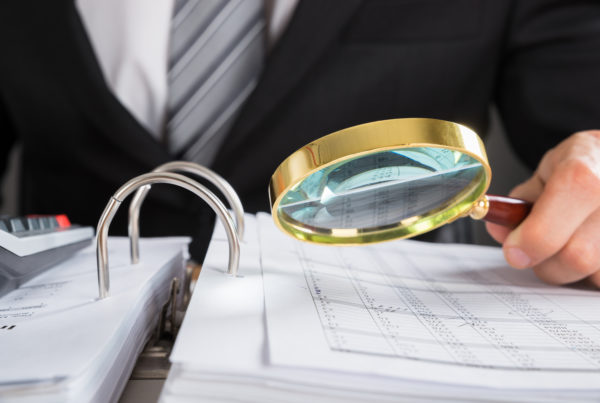 Close-up Of Young Businessman Hand Examining Invoice With Magnifying Glass